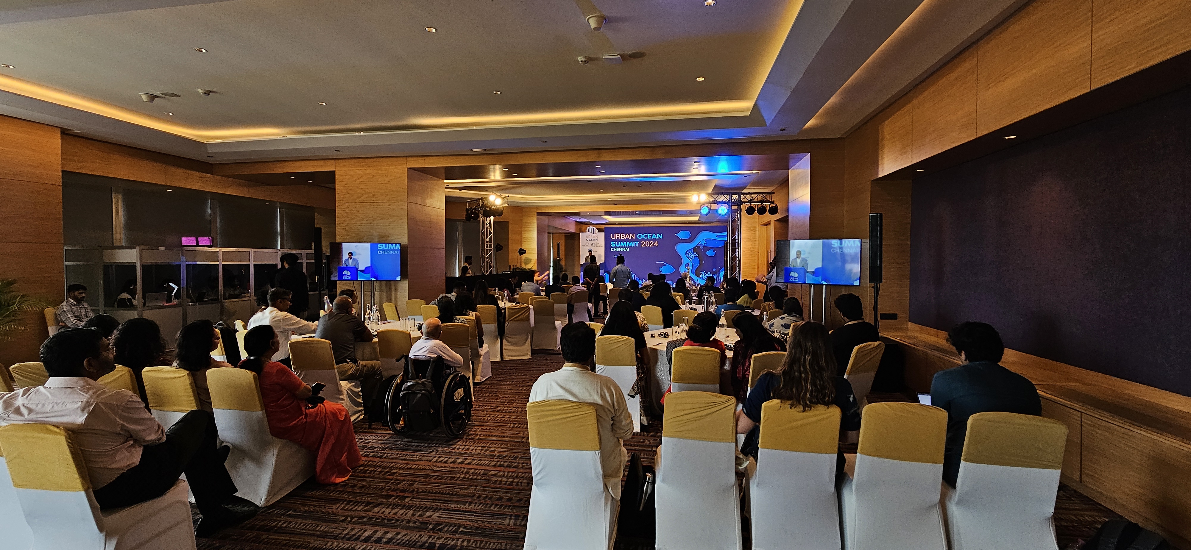 A conference room filled with attendees watching a speaker announce the opening remarks at the Urban Ocean Summit/