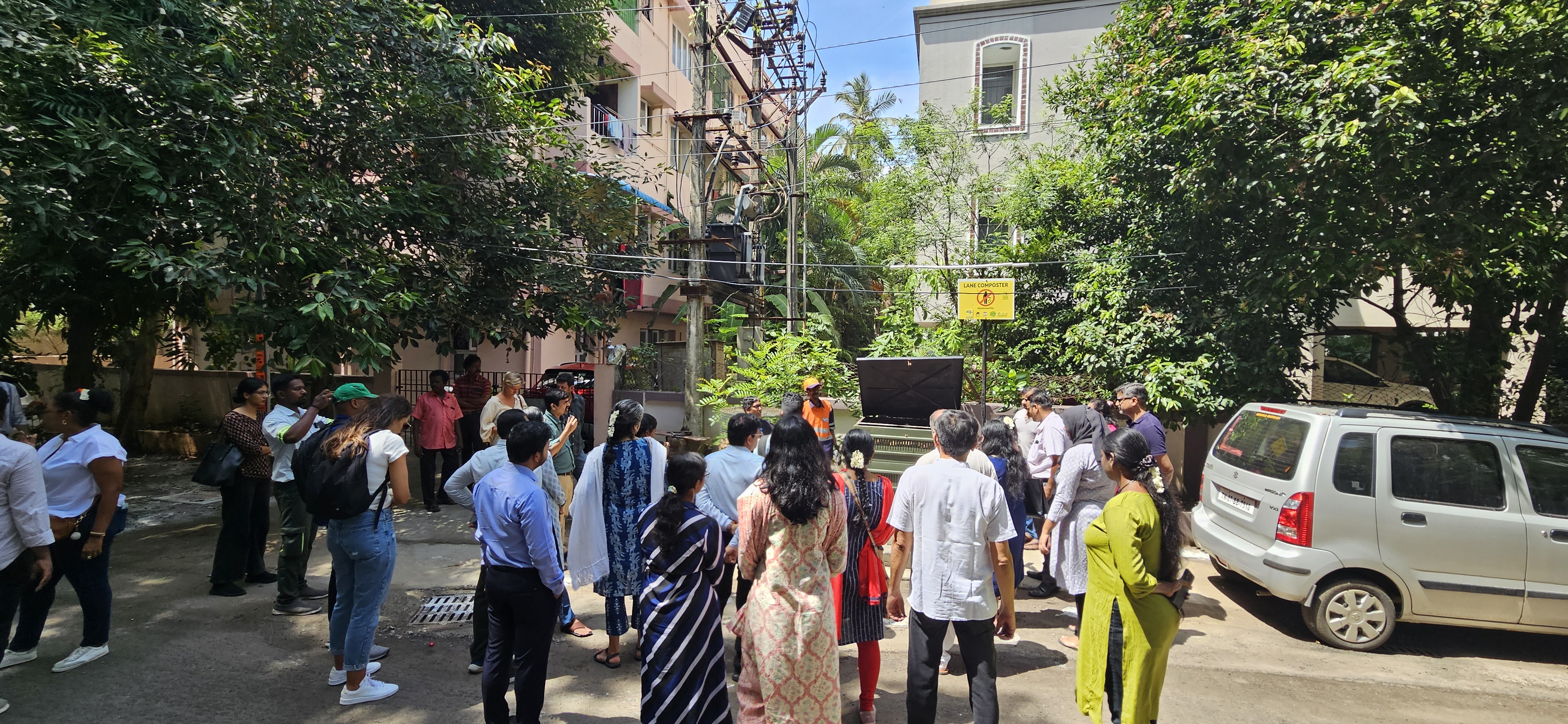 A group of people gathered around a zero-waste neighborhood with urban buildings in the background.