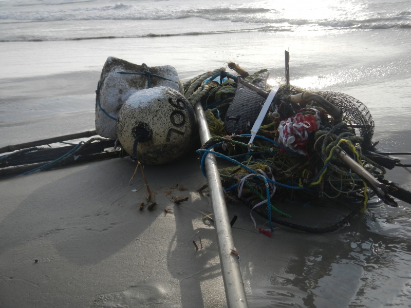 Marine debris, including a metal pole, buoy, and rope, lay tangled on a beach.