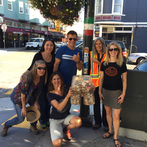 Volunteers hold up a clear plastic bottom filled with cigarette butts next to a butt canister.