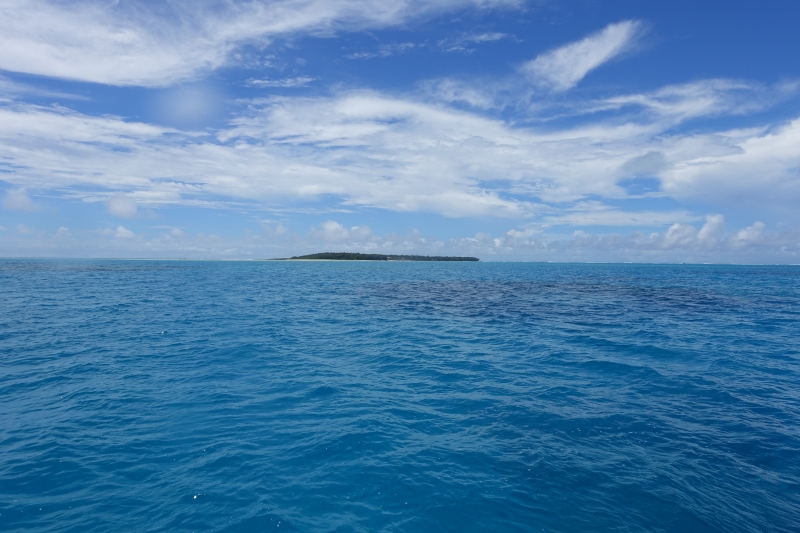 A view of a very blue ocean from the waters surface looking at an island in the distance.