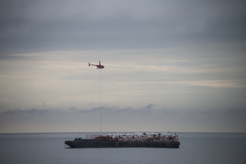 A helicopter flies over a large vessel full of trash.