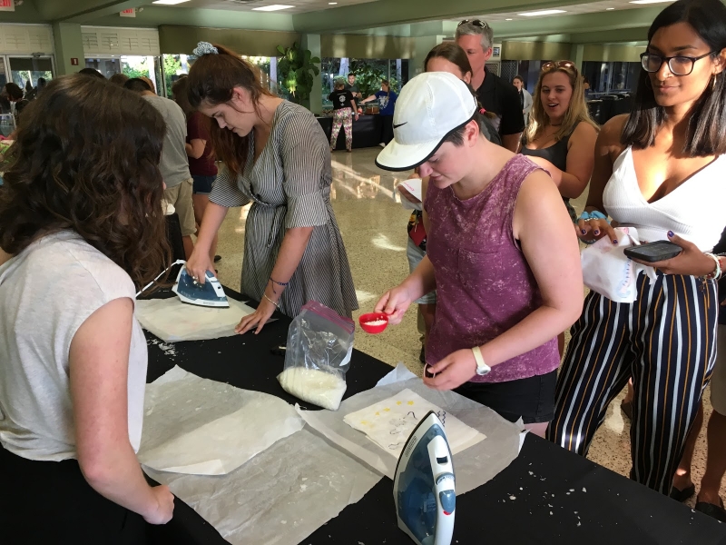 College students iron wax onto sheets of fabric on a table.