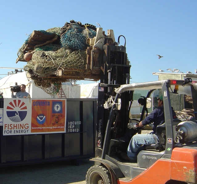 A person uses a forklift to life a large pile of fishing gear into a dumpster.