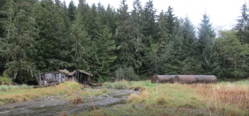 An abandoned float house and two large metal fuel containers.