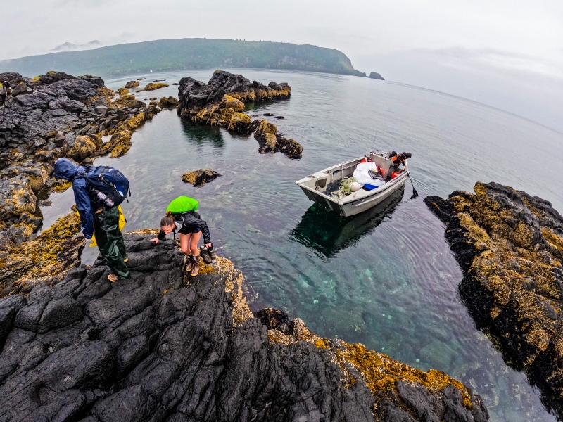 People get off of a small boat in a small rocky inlet.