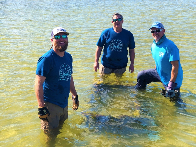Three men smiling in knee deep water.