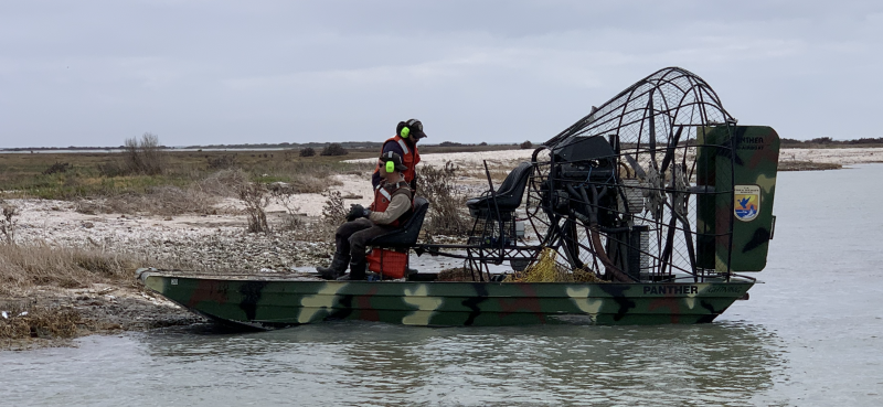 A boat near the shore of a bay with two people aboard and several abandoned crab traps.