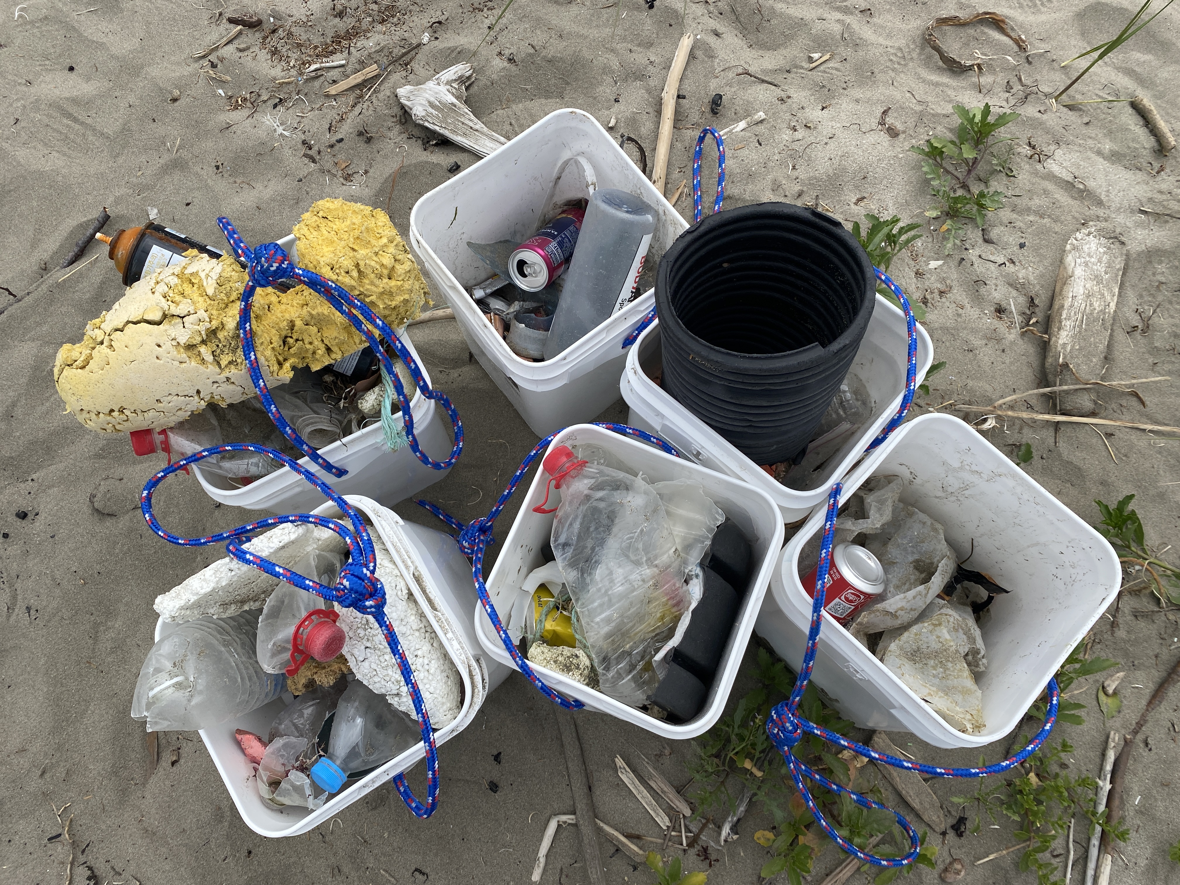Six buckets grouped together and  filled with marine debris collected from a beach cleanup.
