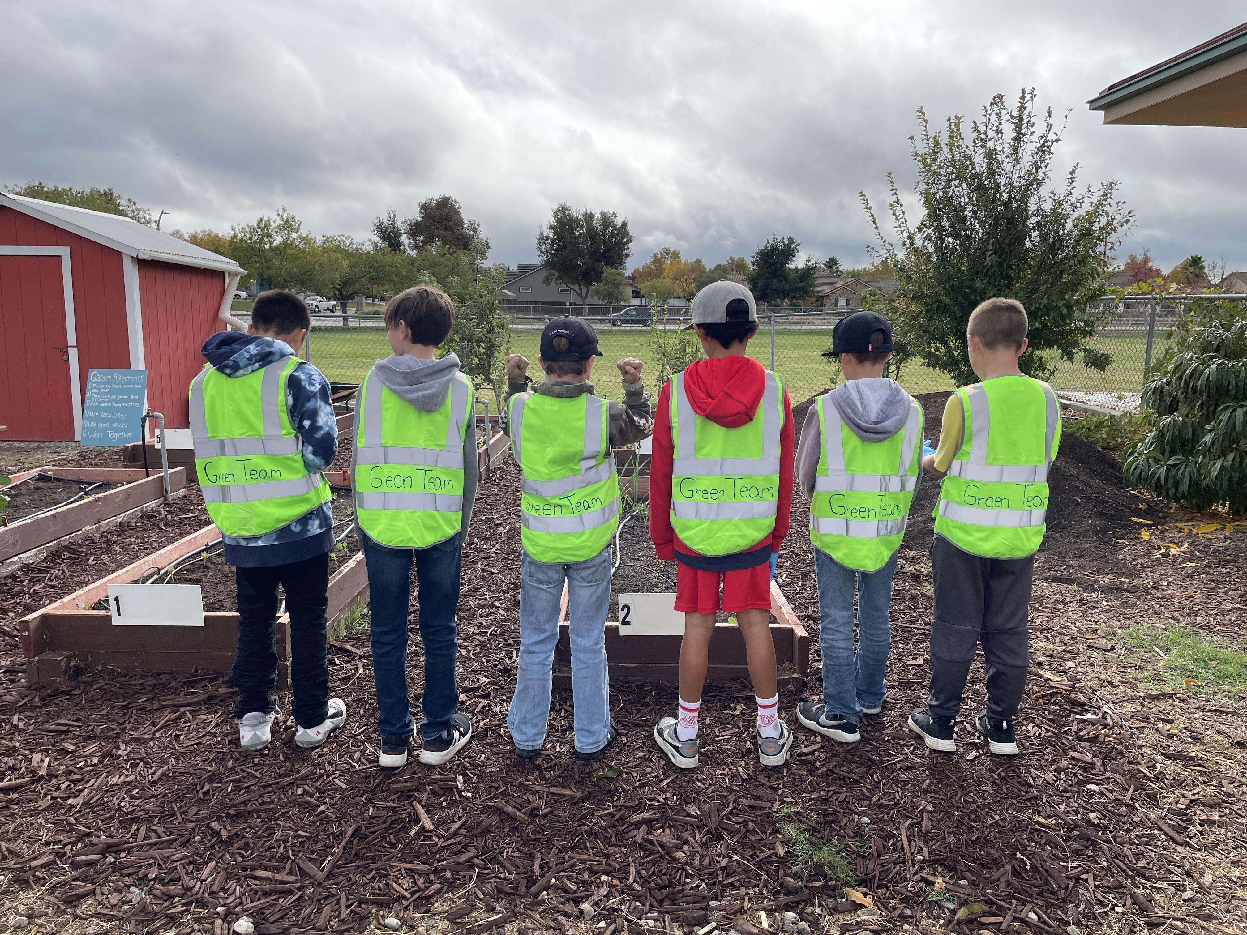 Students wearing safety vests stand shoulder to shoulder facing away from the camera.