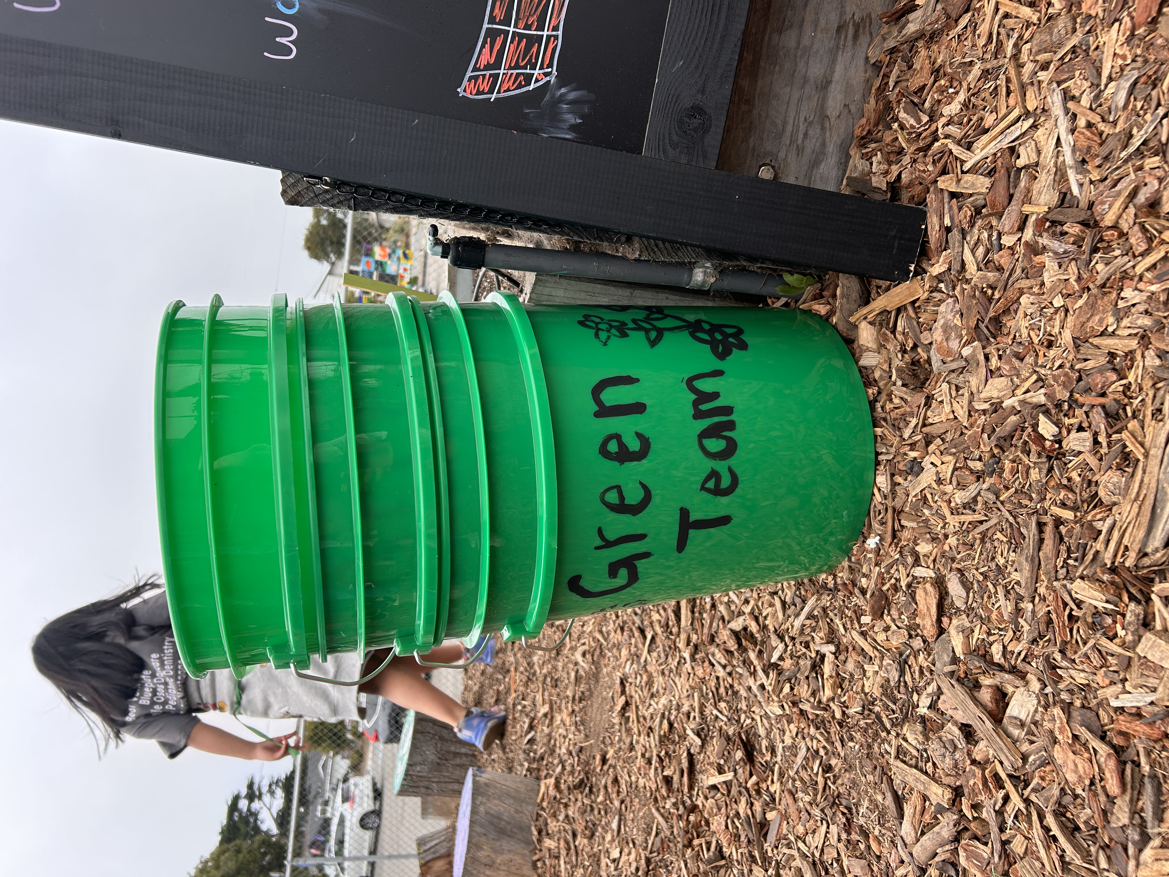 A green bucket with a student walking behind it. 