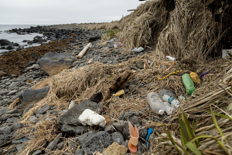 Debris including plastic water bottles and fishing gear piled up along a rocky shoreline.