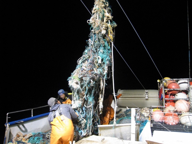 Two people pull up a large fishing net onto a boat.