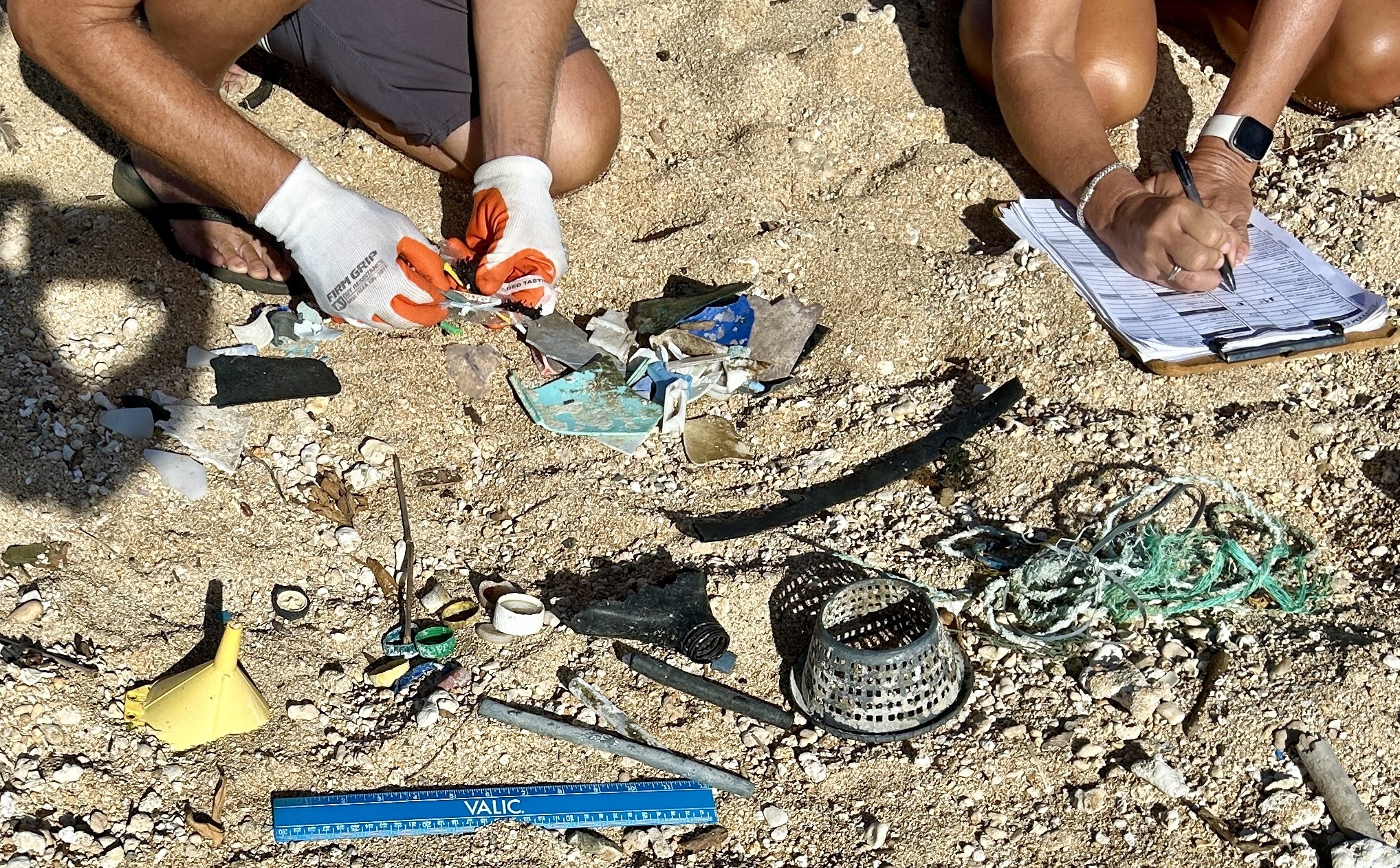Marine debris collected from a cleanup spread out on a sandy beach while two volunteers record what was found on a datasheet.