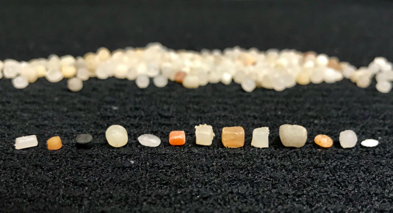 Small plastic pellets of different sizes, shapes, and colors lined up in a row.