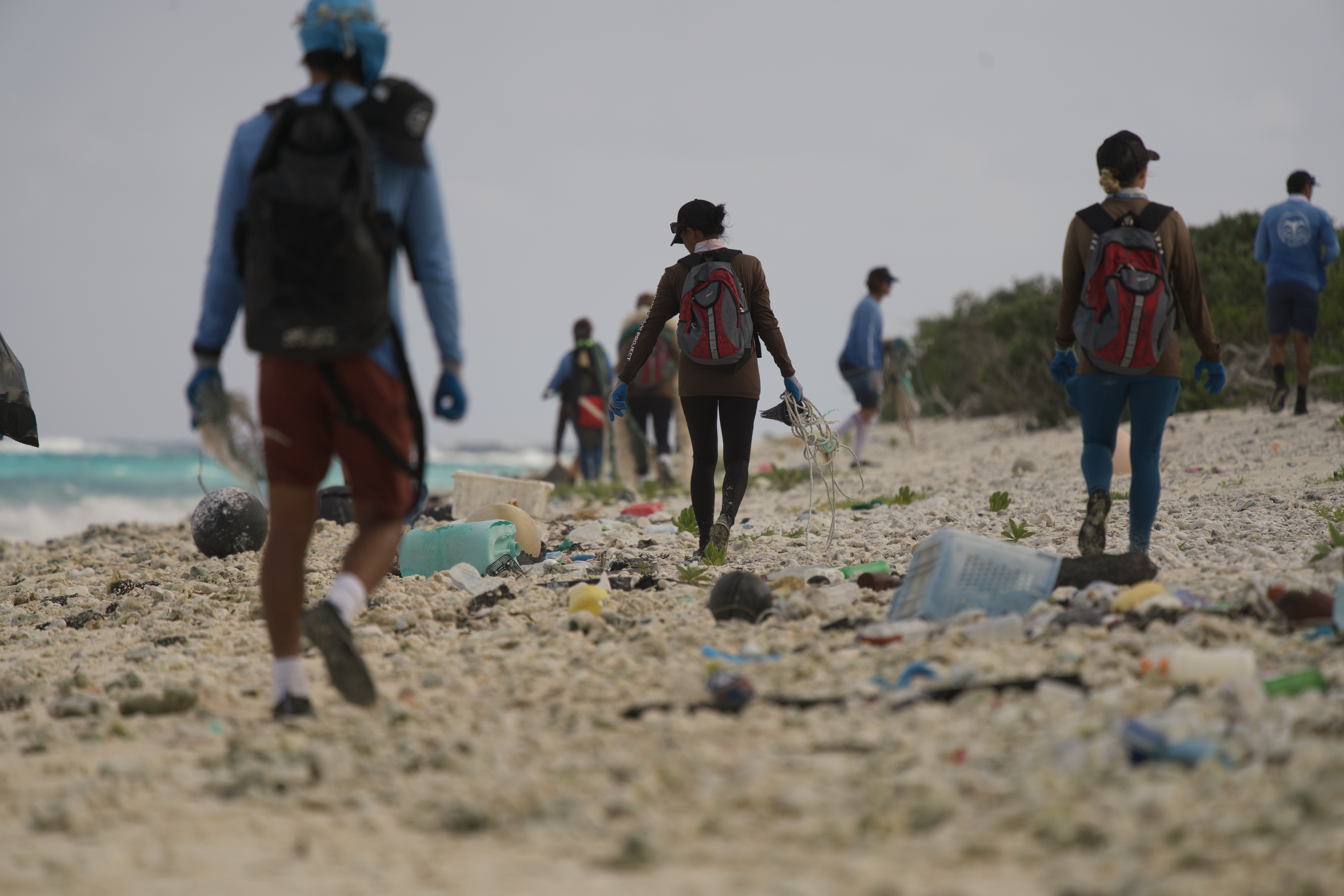 People walk along a beach filled with trash.
