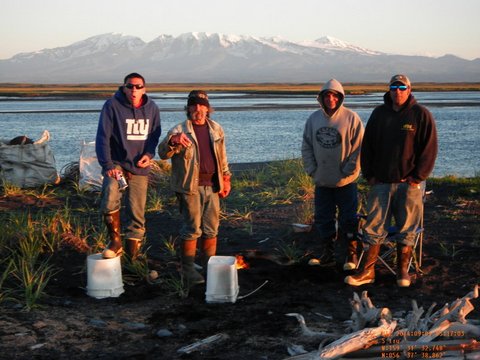 Four men standing in front a river with a snow-capped mountain in the background. 