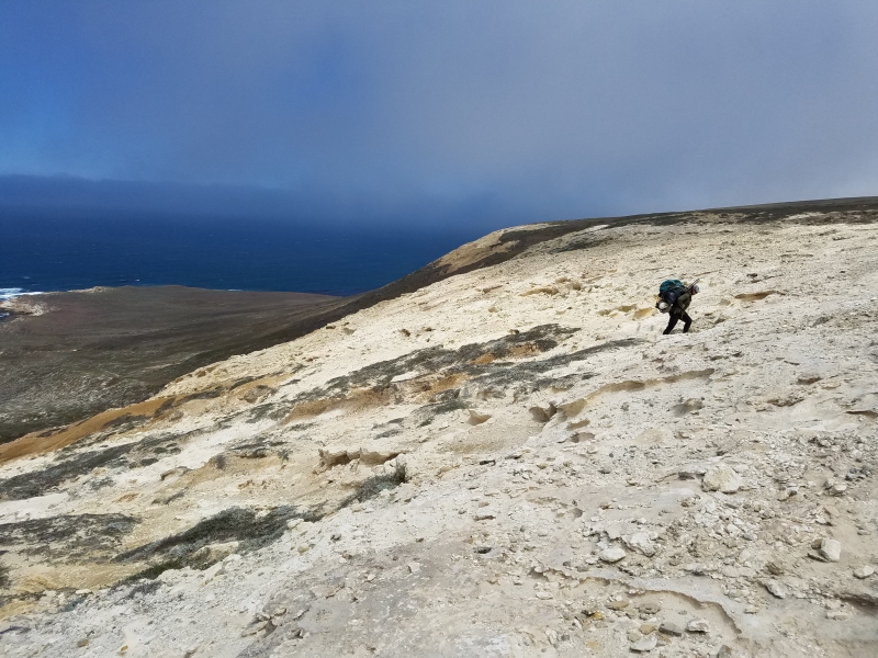 Person hiking up large cliff surrounded by wilderness.