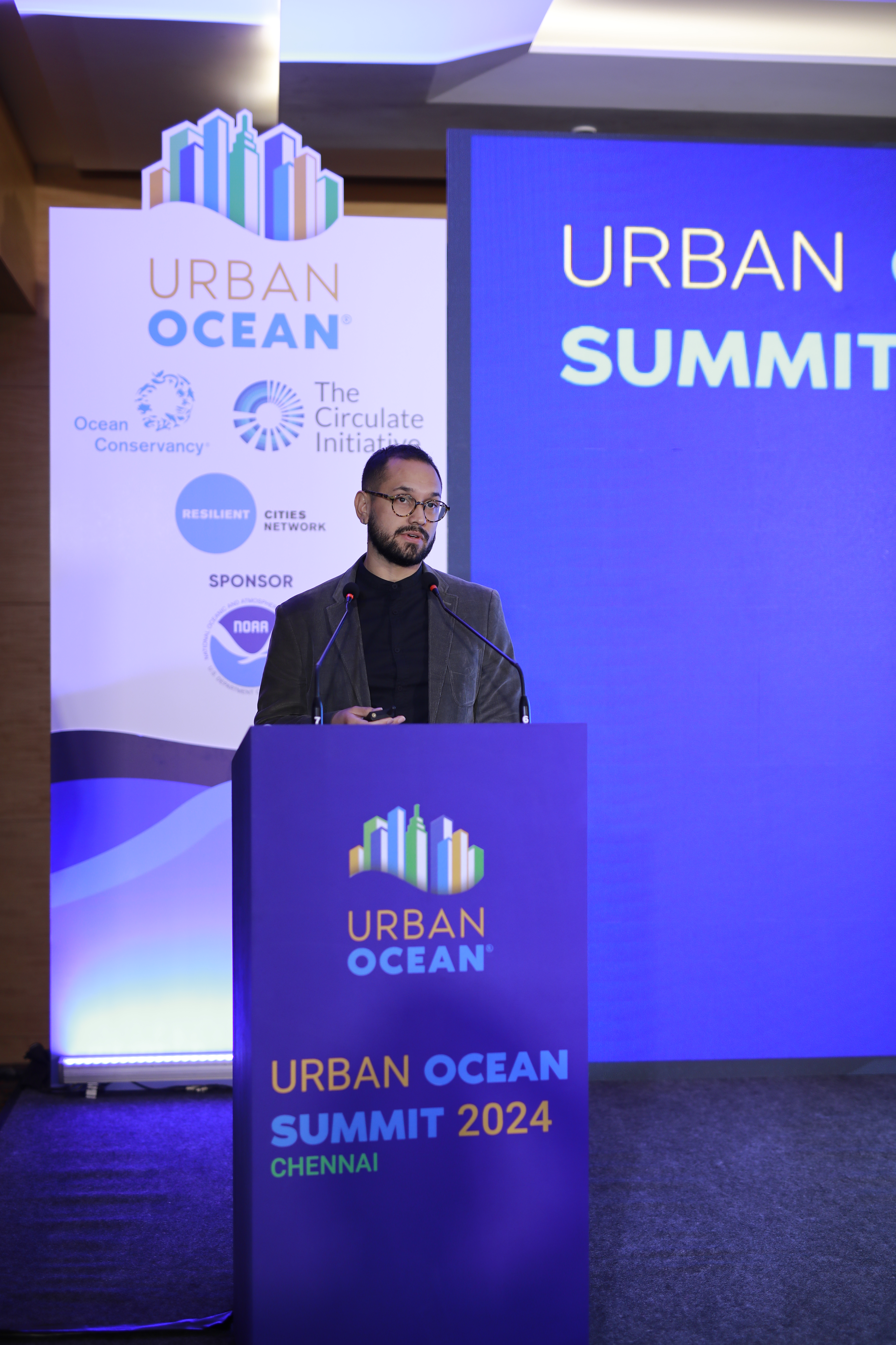A speaker making opening remarks at the Urban Ocean Summit stage.