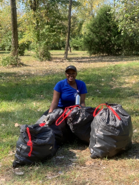 A young person stands behind four full garbage bags that are on the ground.