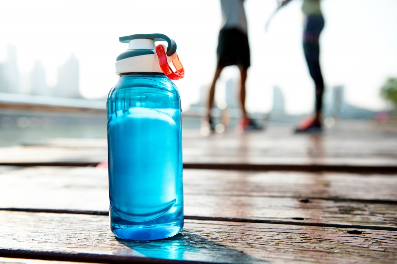 A bottle on wooden slats with two people standing in the distance.