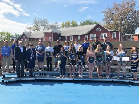 A group standing on bleachers, holding certificates.