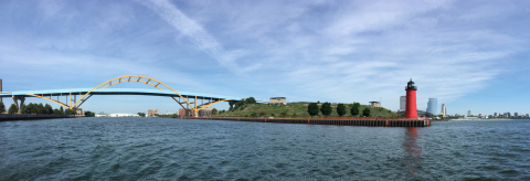 A bridge spanning a river and a red lighthouse at the mouth of a bay.