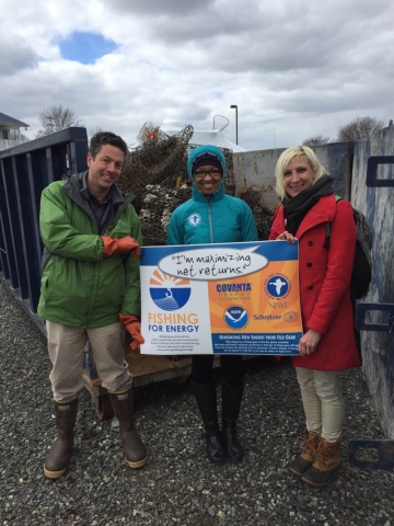 Three people at the event hold a Fishing for Energy sign in front of one of the collection bins.