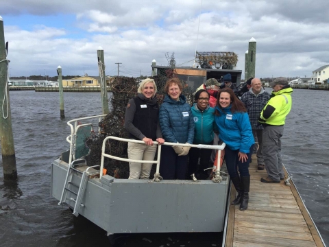 Four event attendees stand on a boat loaded with derelict crab pots.