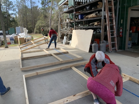 Two people begin to make frames out of 2 X 4 pieces of wood to build a parade float.