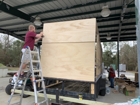 A person nails plywood over a square frame on a parade float.