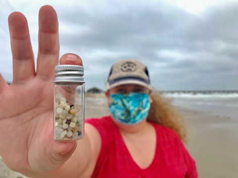 Nurdle Patrol citizen scientist holding up a small jar full of plastic nurdles collected on the beach. 