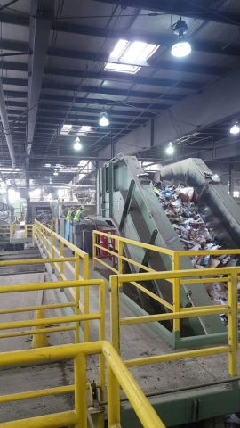 A conveyor belt with recyclable items at a recycling center, with workers in the background.