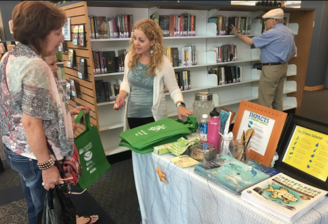 A woman speaking to two people while gesturing to a display table.