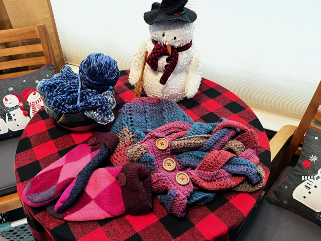A handmade knit hat, scarf, and gloves placed on a table with a plush snowman.