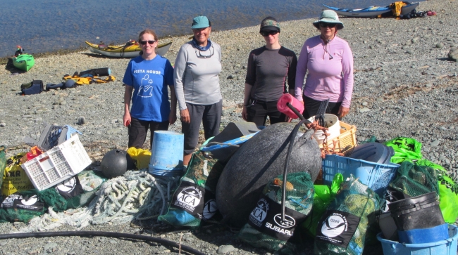 Four people standing on a beach in front of a pile of debris.