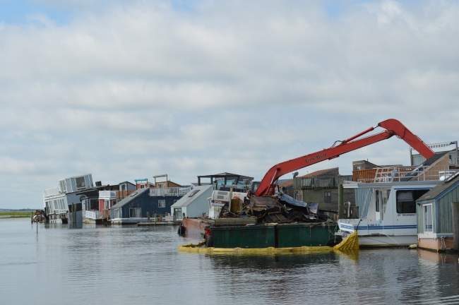 A crane moving debris into a floating dumpster.
