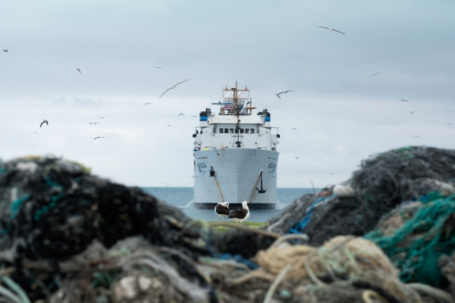 A pile of derelict fishing gear with the NOAA Ship Hi'ialakai in the background.