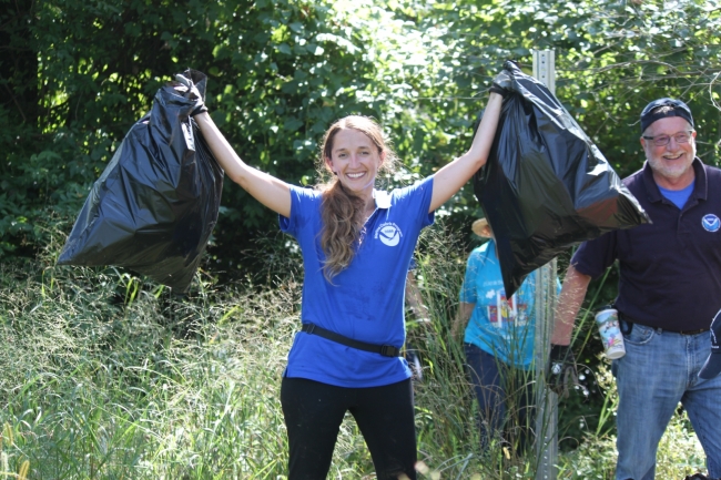 A woman holds up to full garbage bags of collected debris.