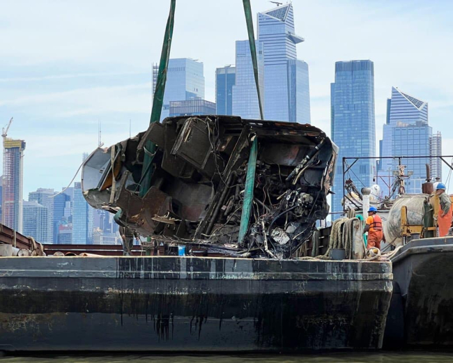 An old, damaged boat getting removed from the water and onto a salvage vessel.