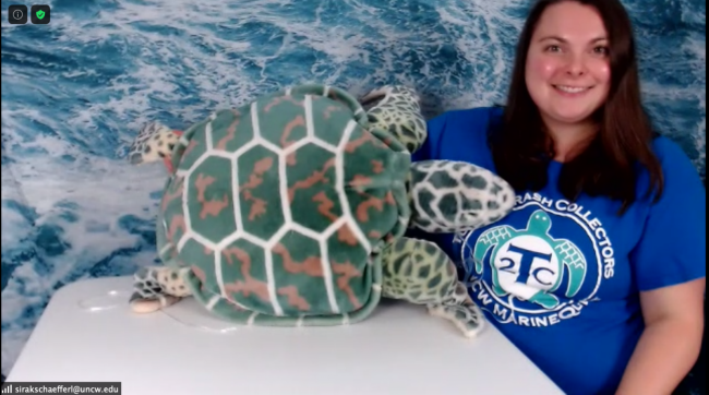 A person sits in a chair and supports a stuffed animal in the shape of a sea turtle on a table.