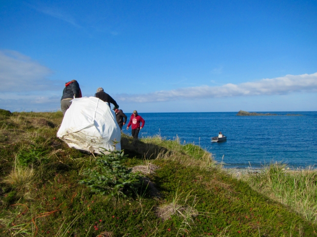People dragging a large bag on debris over a hill.