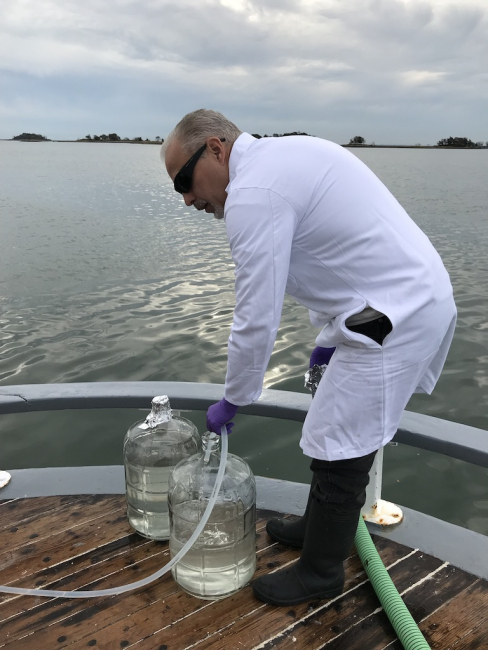 A researcher is pumping water into large glass containers at the back of a vessel.
