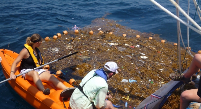 People surrounding floating algae, with debris in it.