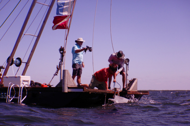 A three-person crew on a barge assisting divers remove debris from the water.