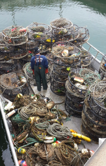 A person standing on a boat, surrounded by lots of derelict crab traps and ropes.