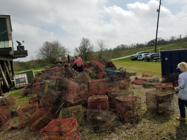Two people stand to look at a huge pile of collected crab pots. 