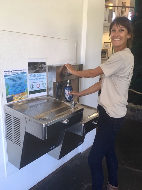 A person smiles while filling up a water bottle at a filling station.