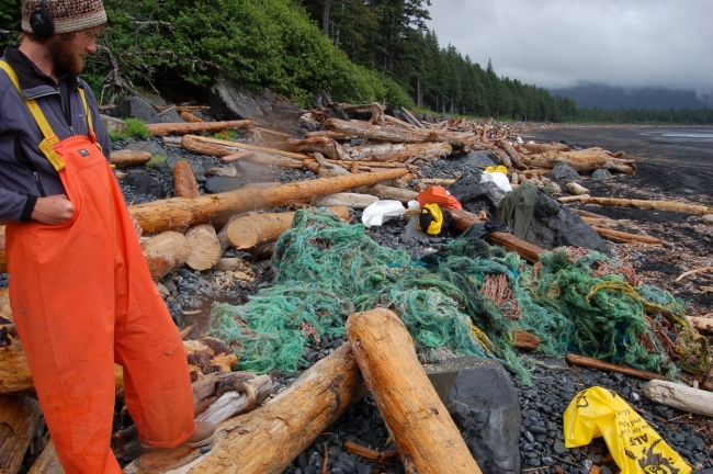 A man looks down on marine debris along a rugged Alaskan beach. 