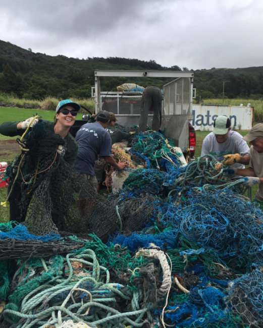 A person smiles while holding up a dark green and very large fishing net.